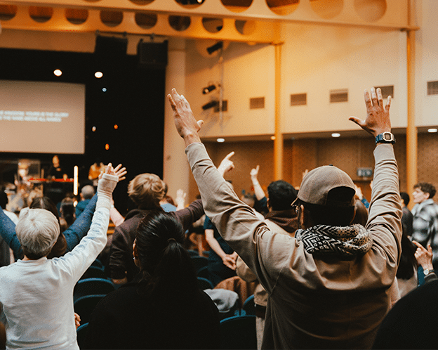 People at a church service, standing for sung worship, some with raised hands.